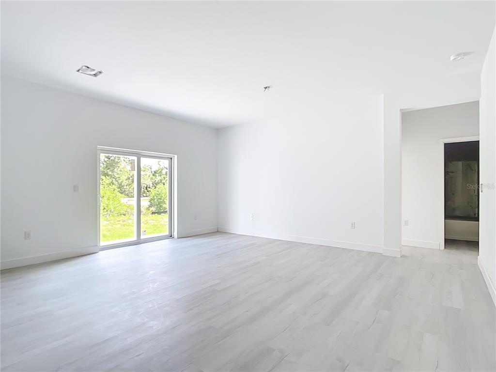 A bright, empty room features light-colored wood flooring, white walls, and a sliding glass door — 16134 LIBOURN AVENUE, PORT CHARLOTTE, FL