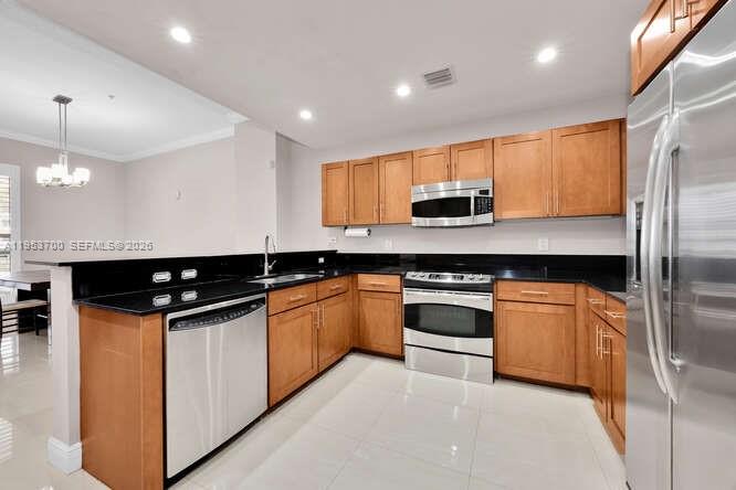 A kitchen features light wood cabinets, black countertops, and stainless steel appliances — 8395 SW 73rd Ave # 104, Miami FL 33143, MIAMI, FL