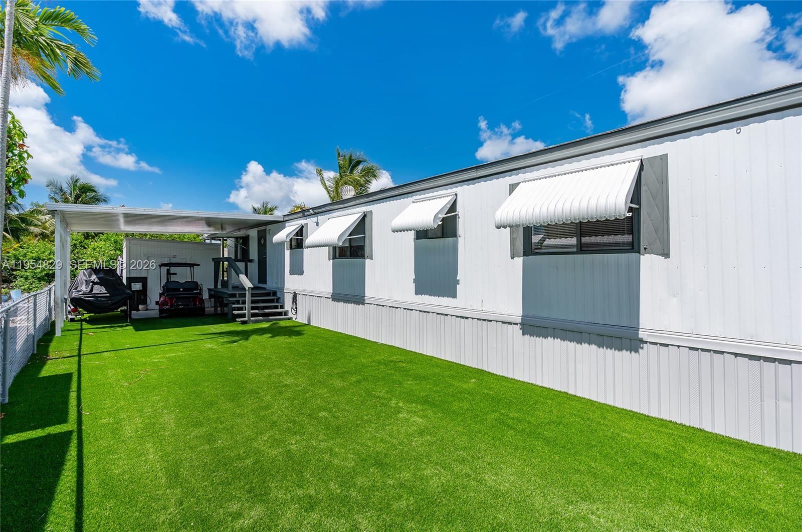 A white mobile home with a green lawn, carport, and golf cart under a blue sky — 456 Bowie Ln # 456, Key Largo FL 33037, KEY LARGO, FL