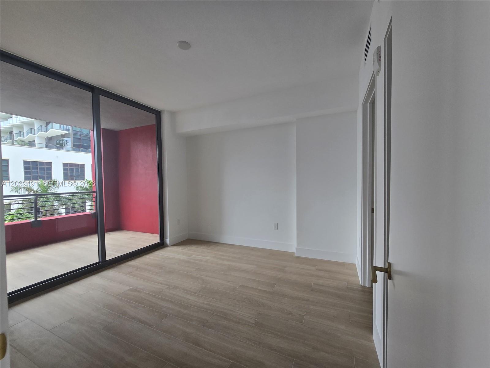 An empty room features light wood-look flooring, white walls, and a sliding glass door to a balcony — 90 NE 32ND ST # 305, Miami FL 33137, MIAMI, FL