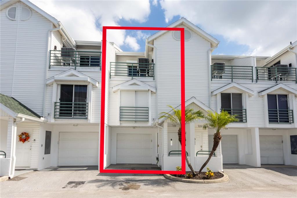 A three-story white townhouse exterior with a garage, a second-floor balcony, and a third-floor deck — 320 ISLAND WAY UNIT 605, CLEARWATER BEACH, FL