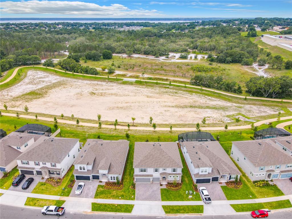 An aerial view shows a row of suburban houses facing a large, undeveloped sandy lot — 4379 RENLY LANE, CLERMONT, FL