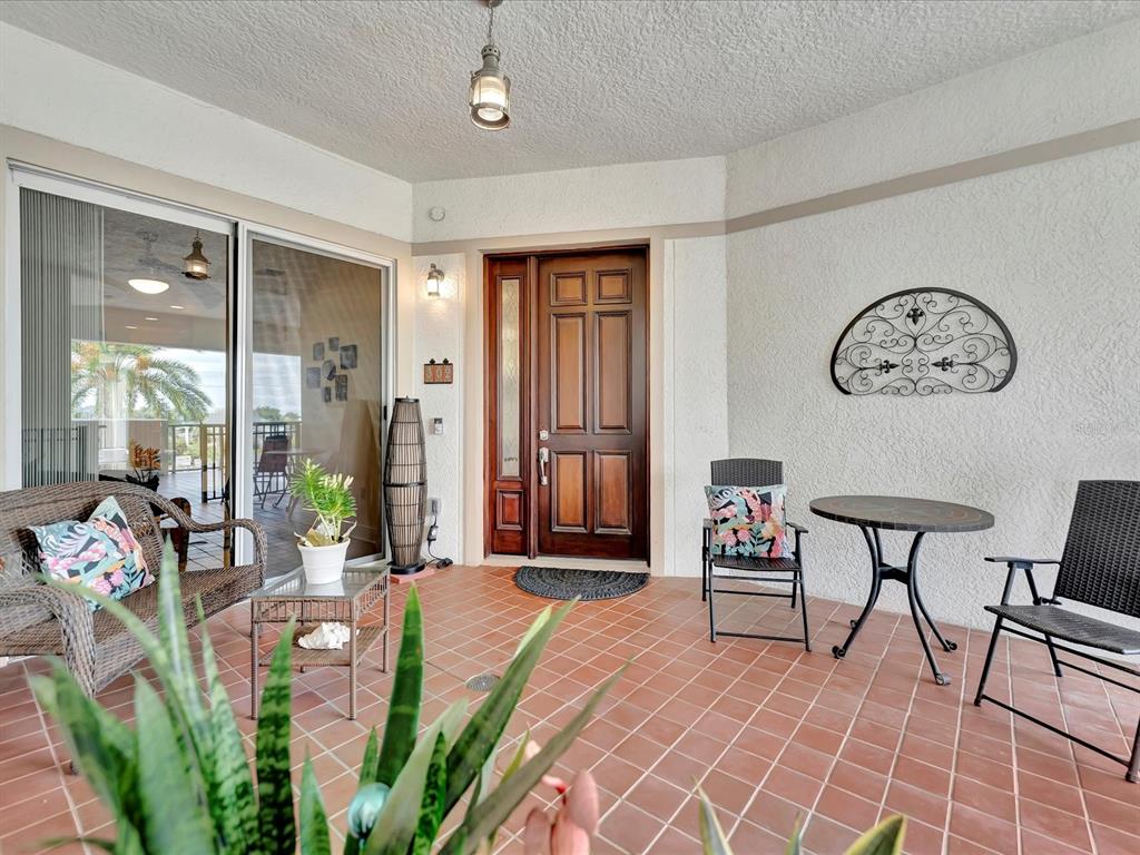 A covered patio features tiled flooring, a wooden front door, and outdoor furniture — 1022 BELLASOL WAY UNIT 5302, APOLLO BEACH, FL