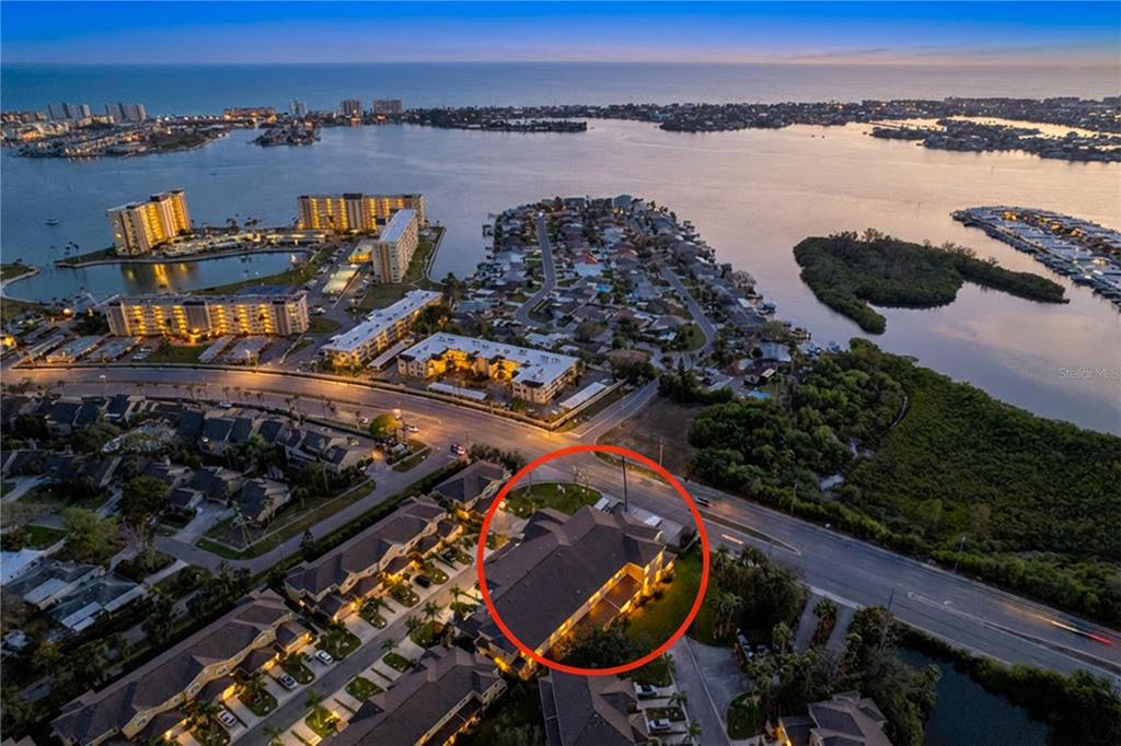 An aerial view shows a residential building highlighted by a red circle near a road — 11273 KAPOK GRAND CIRCLE, MADEIRA BEACH, FL