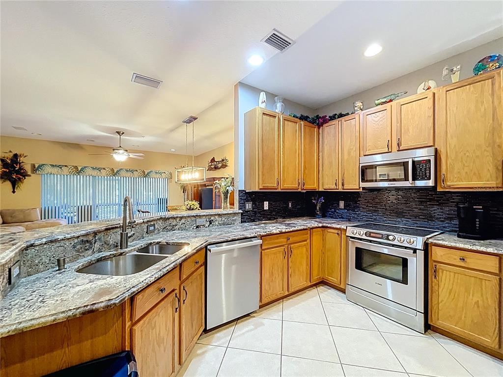 A kitchen features oak cabinets, granite countertops, stainless steel appliances, and a tiled floor — 11273 KAPOK GRAND CIRCLE, MADEIRA BEACH, FL
