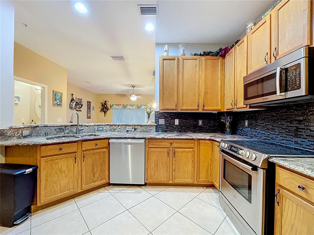 A kitchen features oak cabinets, granite countertops, stainless steel appliances, and a dark tile backsplash — 11273 KAPOK GRAND CIRCLE, MADEIRA BEACH, FL