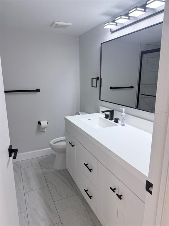 A modern bathroom features a white vanity, black hardware, a rectangular mirror, and gray flooring — 3300 COVE CAY DRIVE UNIT 2A, CLEARWATER, FL