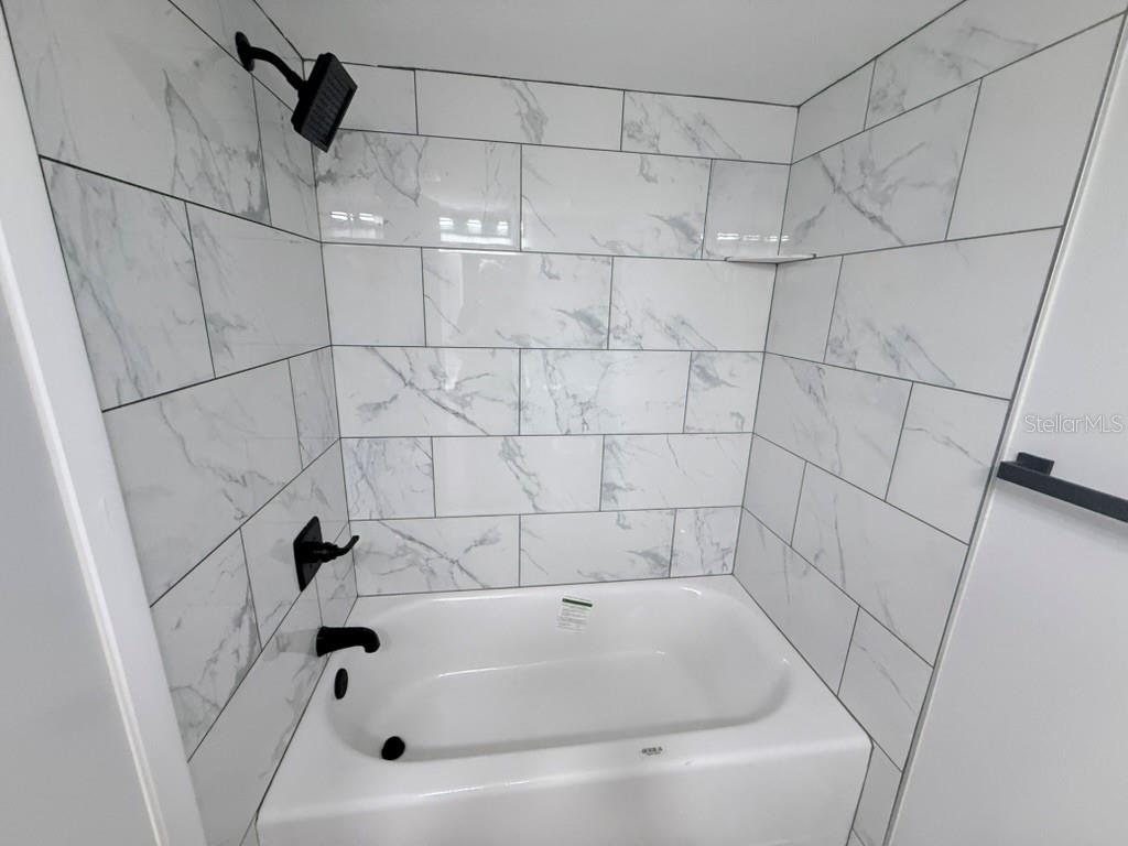 A bathroom features a white bathtub with a marble-look tiled surround and black fixtures — 3300 COVE CAY DRIVE UNIT 2A, CLEARWATER, FL