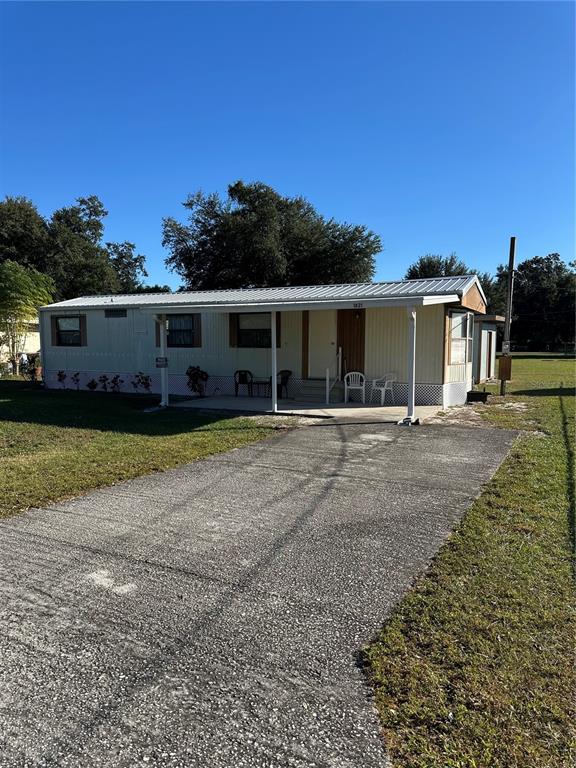 A single-story mobile home features a metal roof, a covered porch, and a concrete driveway — 1821 FRUITLAND PARK CIRCLE, EAGLE LAKE, FL