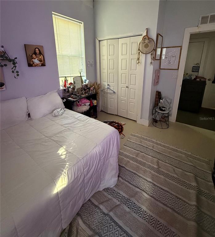 A bedroom features a white bed, a patterned rug, a closet, and lavender-colored walls — 727 NW 4TH AVENUE, GAINESVILLE, FL