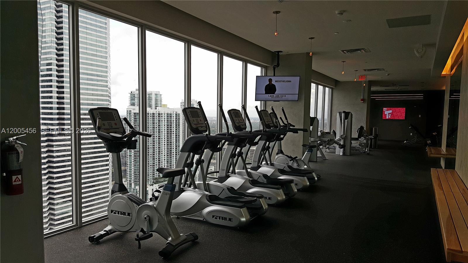 A gym features rows of exercise equipment facing floor-to-ceiling windows overlooking a city skyline — 151 SE 1st St # 1609, Miami FL 33131, MIAMI, FL