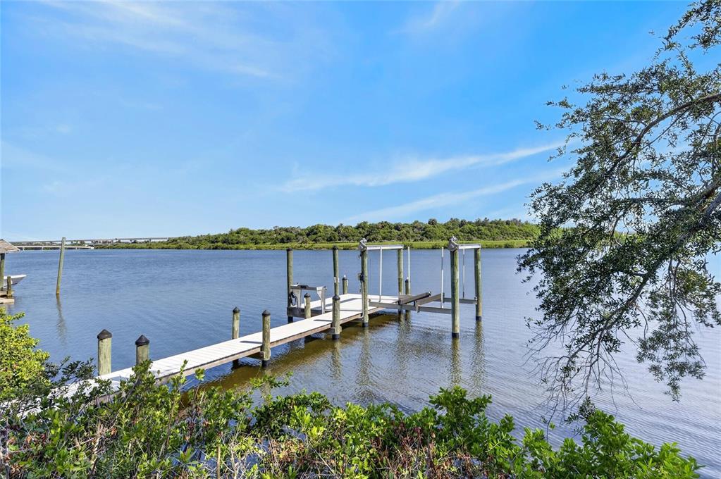 A wooden dock with a boat lift extends into a calm river under a blue sky — 6712 MYRNA DRIVE, TAMPA, FL