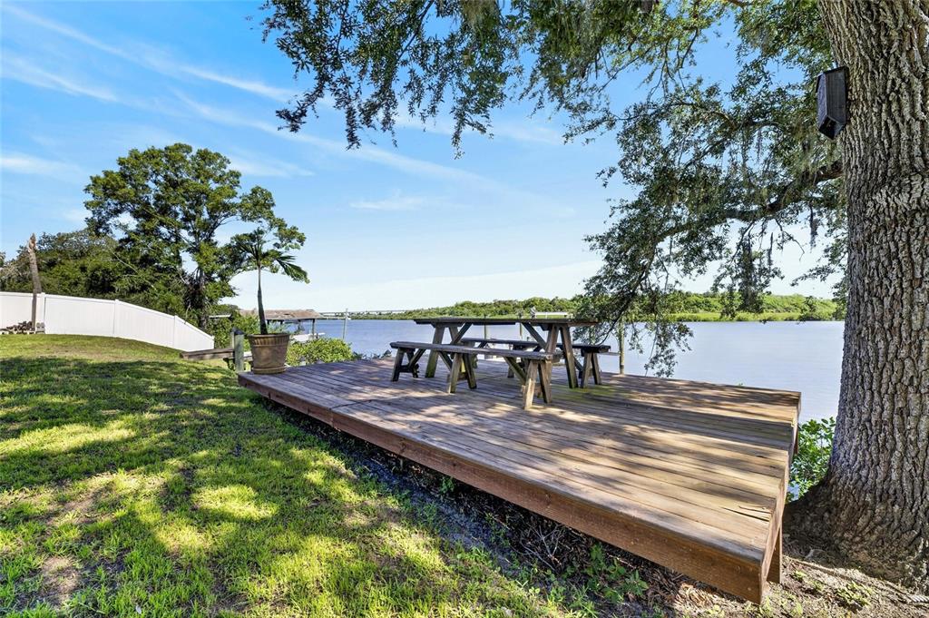 A wooden deck with a picnic table overlooks a river under a large oak tree — 6712 MYRNA DRIVE, TAMPA, FL