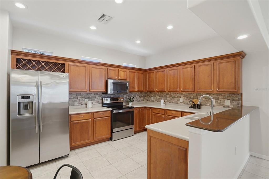 A kitchen with wood cabinets, stainless steel appliances, and a stone tile backsplash — 8005 SHADDOCK PLACE, LAND O LAKES, FL