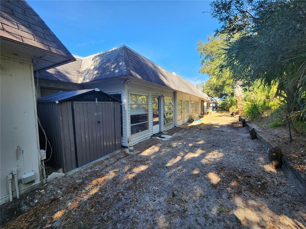 The exterior of a house features a metal storage shed and a sandy backyard area — 4230 SHELDON PLACE UNIT 4230, NEW PORT RICHEY, FL