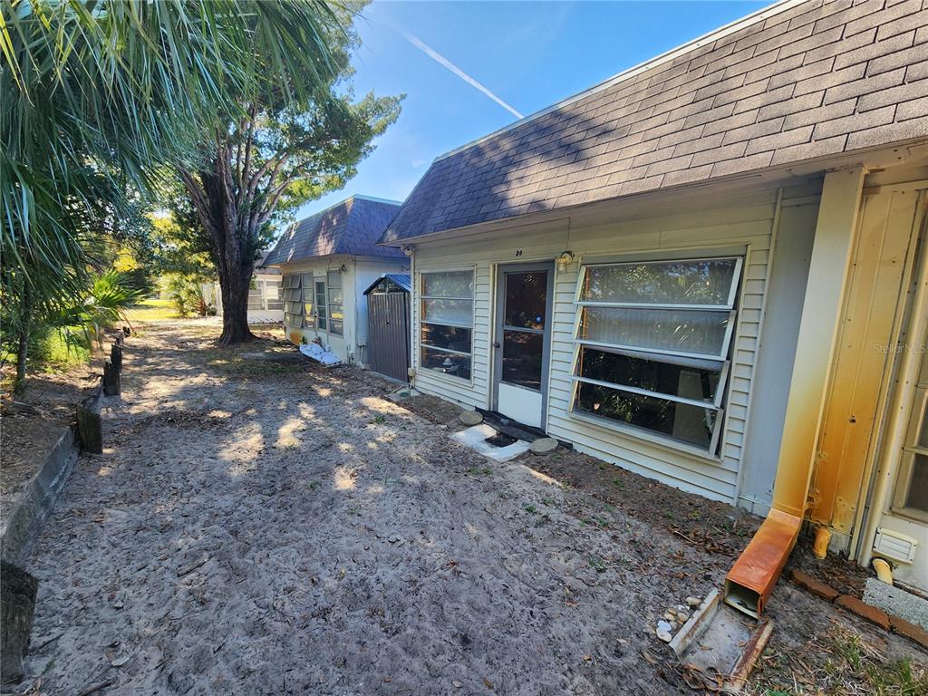 Exterior view of a small house with a sandy yard, metal shed, and metal awning windows — 4230 SHELDON PLACE UNIT 4230, NEW PORT RICHEY, FL