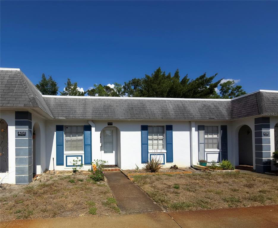 A single-story residential building features white stucco walls, blue shutters, and a gray shingled roof — 4230 SHELDON PLACE UNIT 4230, NEW PORT RICHEY, FL