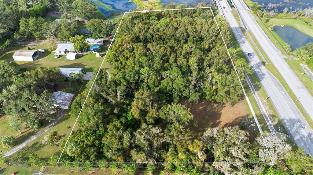 An aerial view shows a wooded, rectangular plot of land adjacent to a highway — 214 W INTERNATIONAL SPEEDWAY BOULEVARD, DELAND, FL