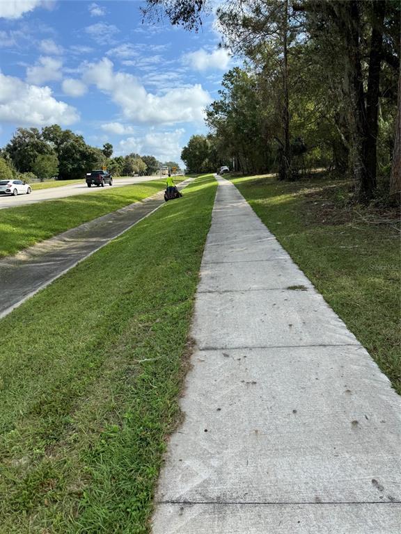 A concrete sidewalk runs alongside a grassy embankment and a road with passing vehicles — 214 W INTERNATIONAL SPEEDWAY BOULEVARD, DELAND, FL