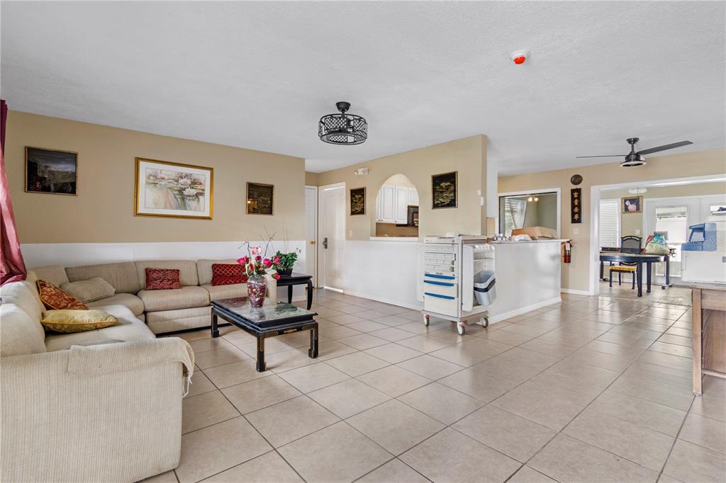A living room with beige tile floors, a sectional sofa, and an open kitchen area — 1029 PINE RIDGE CIRCLE, BRANDON, FL