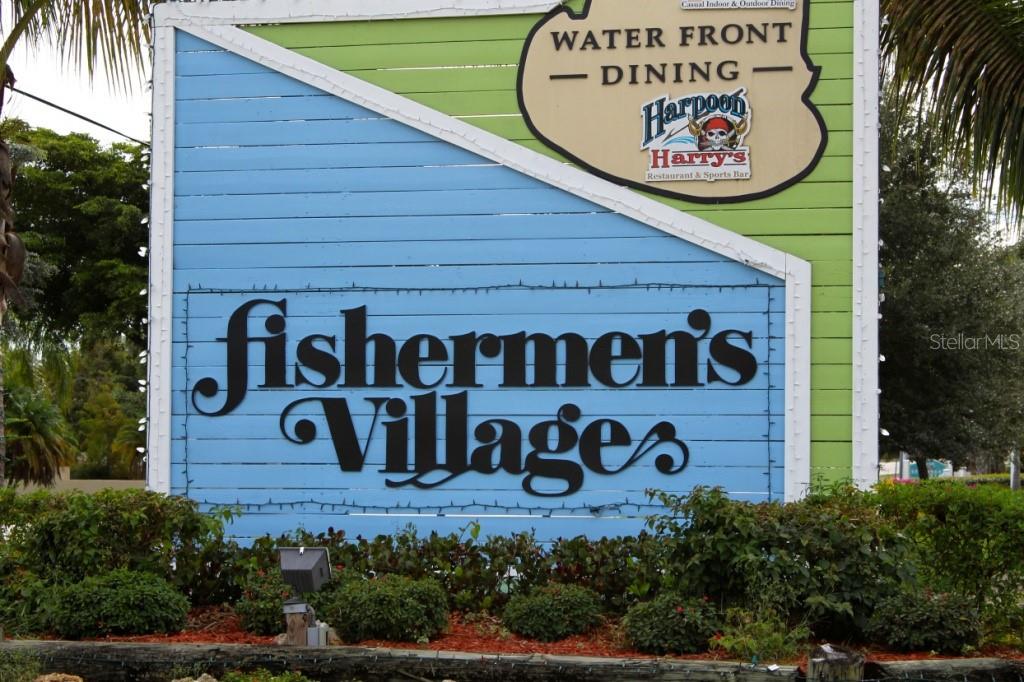 A large, blue and green wooden sign for Fishermen's Village stands outdoors near landscaping — 2267 CANNOLOT BOULEVARD, PORT CHARLOTTE, FL