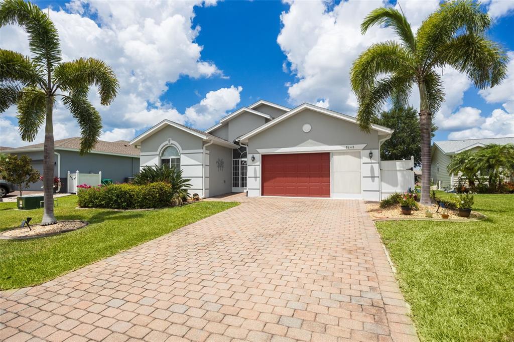A single-story house with a red garage door, paved driveway, and palm trees — 8648 LAKE FRONT COURT, PUNTA GORDA, FL