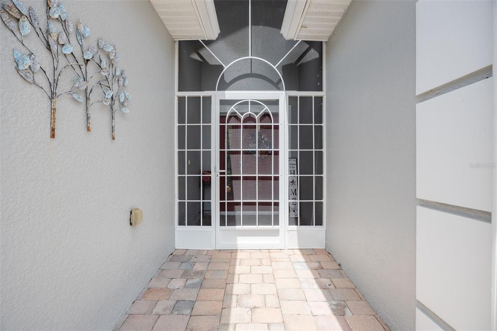 A covered entryway features a white storm door with a decorative arch and paver flooring — 8648 LAKE FRONT COURT, PUNTA GORDA, FL