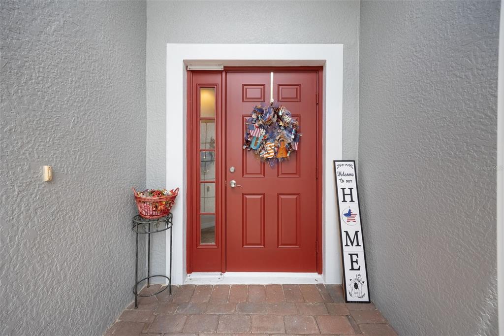 A red front door with a sidelight, patriotic wreath, and a welcome sign on a porch — 8648 LAKE FRONT COURT, PUNTA GORDA, FL
