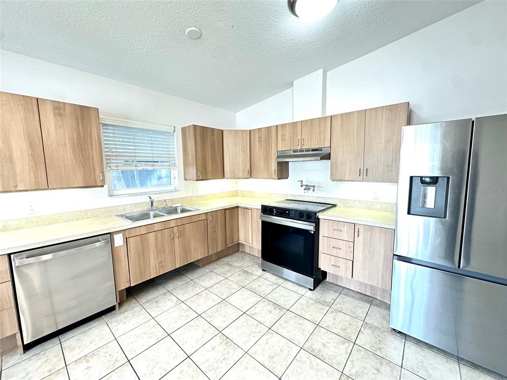 A kitchen features light wood cabinets, stainless steel appliances, a double sink, and tiled flooring — 1121 DR MARTIN LUTHER KING JR STREET S, ST PETERSBURG, FL