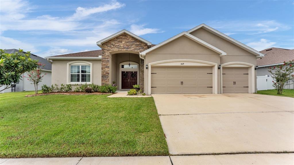 A single-story house with a stone-accented entrance, tan stucco exterior, and a three-car garage — 4129 TIMBER VALLEY WAY, LAKELAND, FL