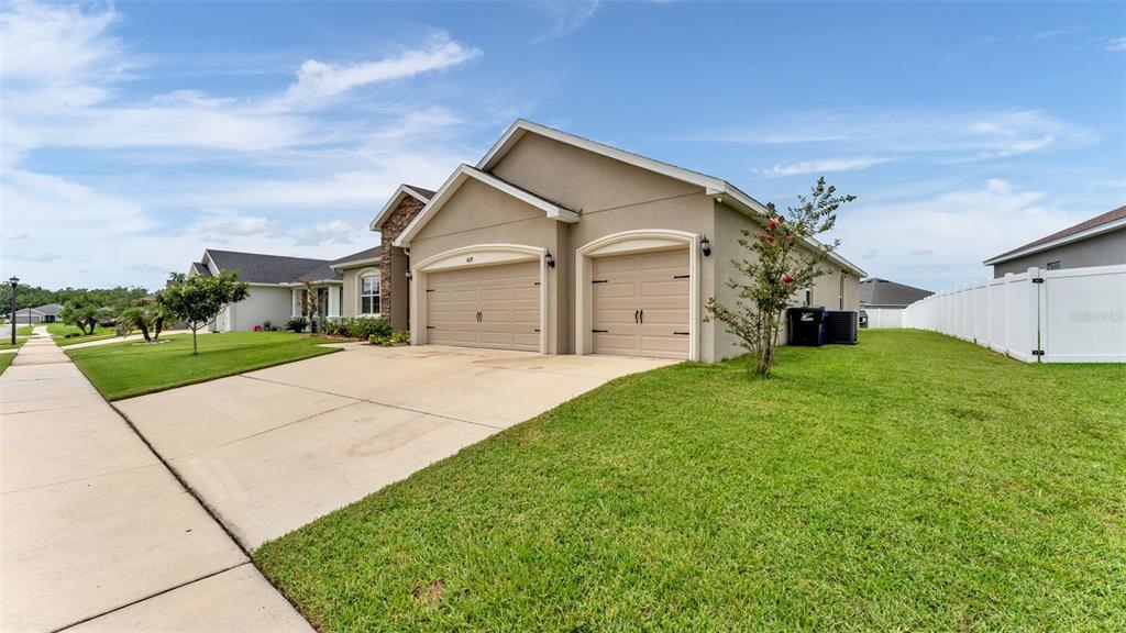 A single-story house with a beige stucco exterior, a three-car garage, and a white fence — 4129 TIMBER VALLEY WAY, LAKELAND, FL