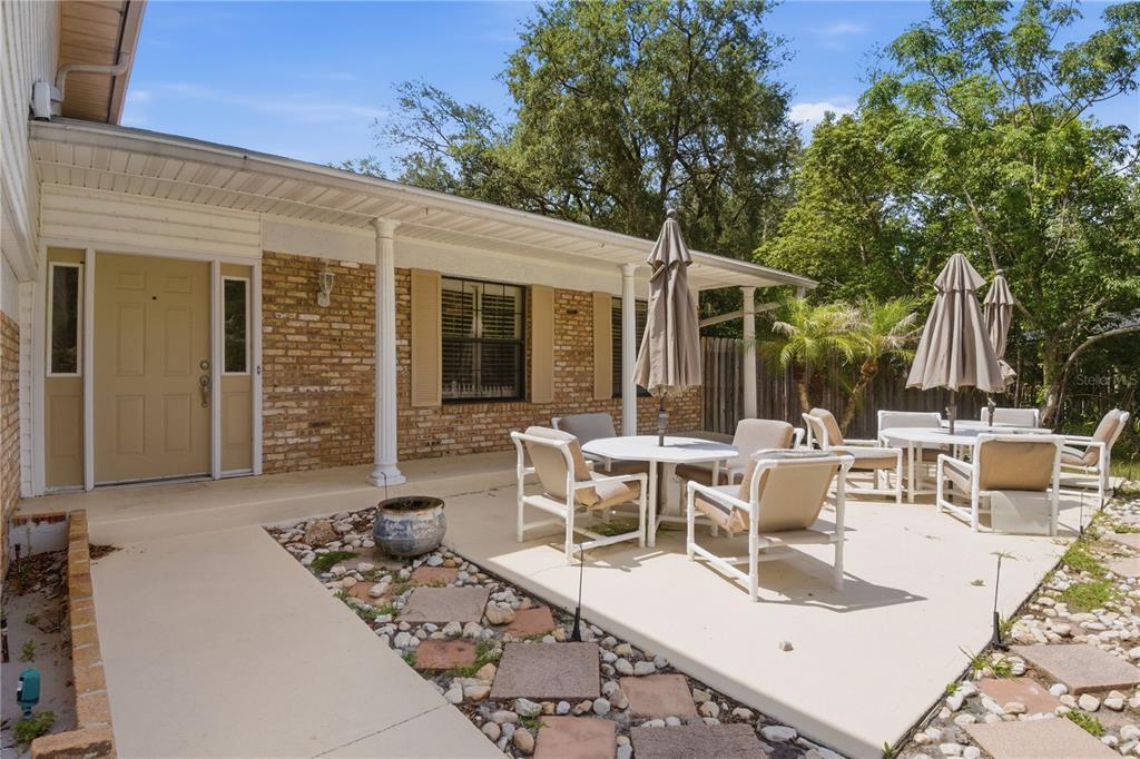 A patio with outdoor furniture and umbrellas sits in front of a brick house exterior — 1204 SWAN STREET, WINTER SPRINGS, FL