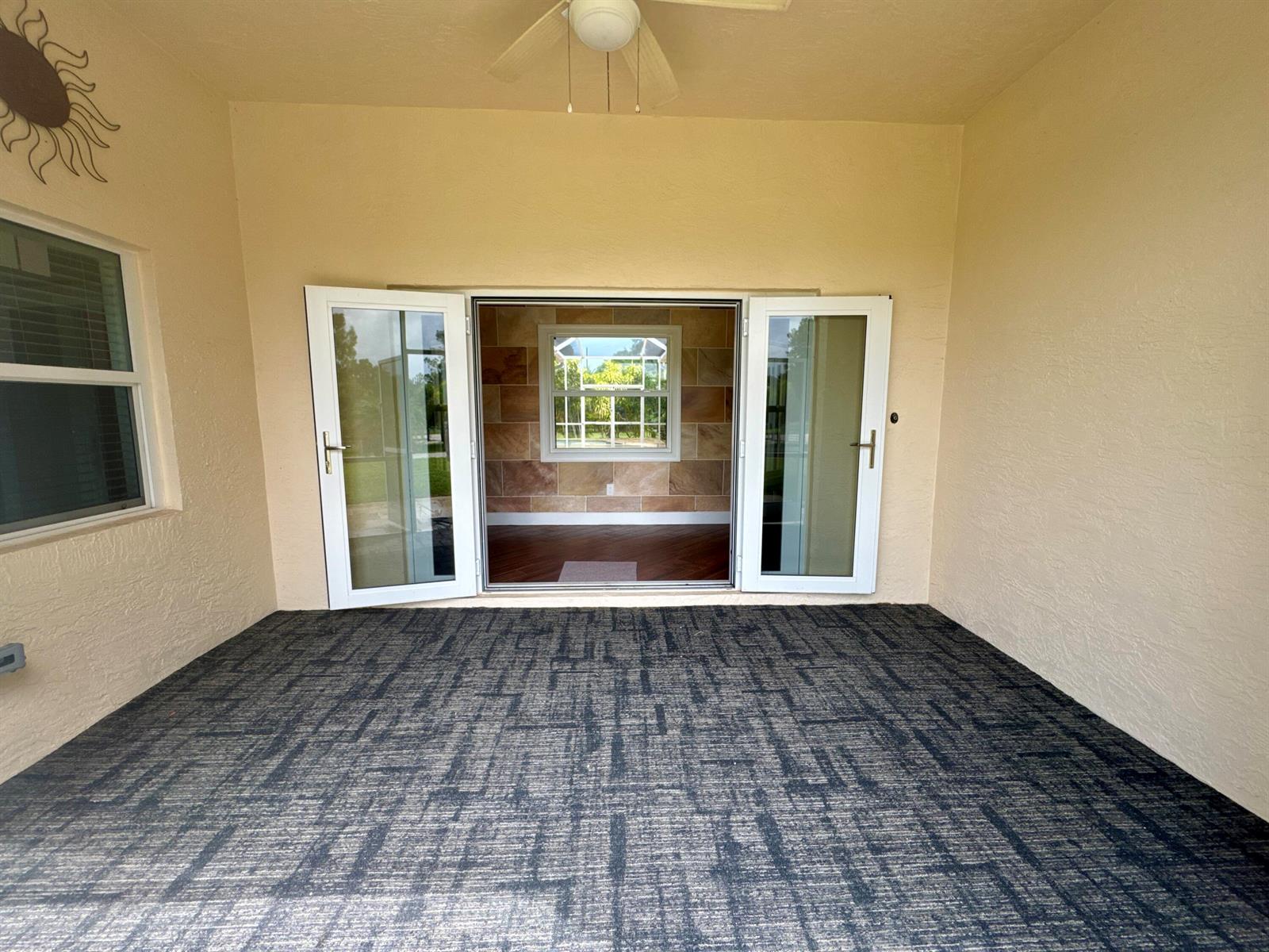 A covered patio with dark patterned carpeting leads through French doors into an interior room — 14717 11th Terrace, FL 33470, FL
