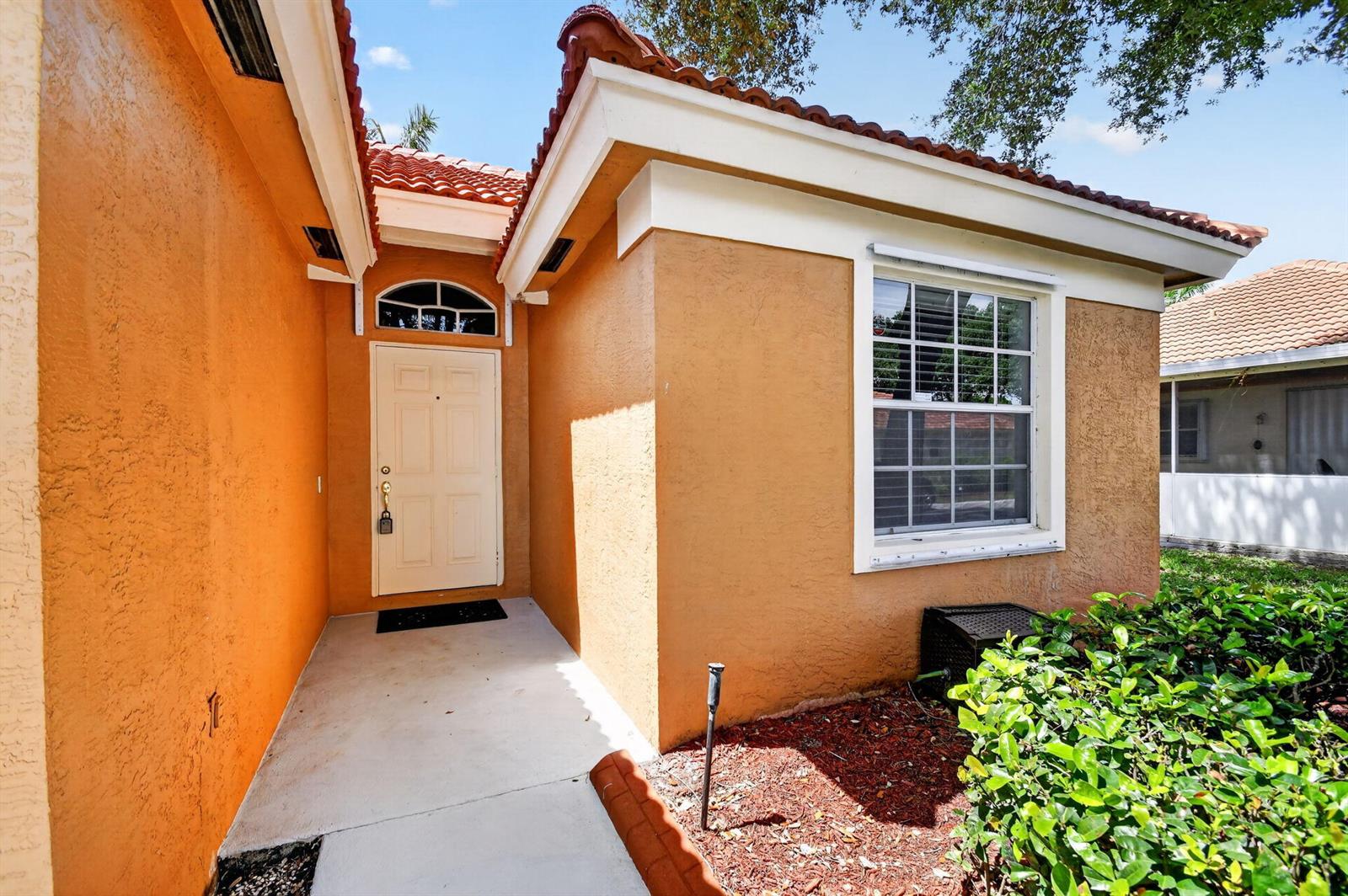 The exterior of a house features orange stucco walls, a tiled roof, and a front door — 1084 Aspri Way, Riviera Beach FL 33418, RIVIERA BEACH, FL