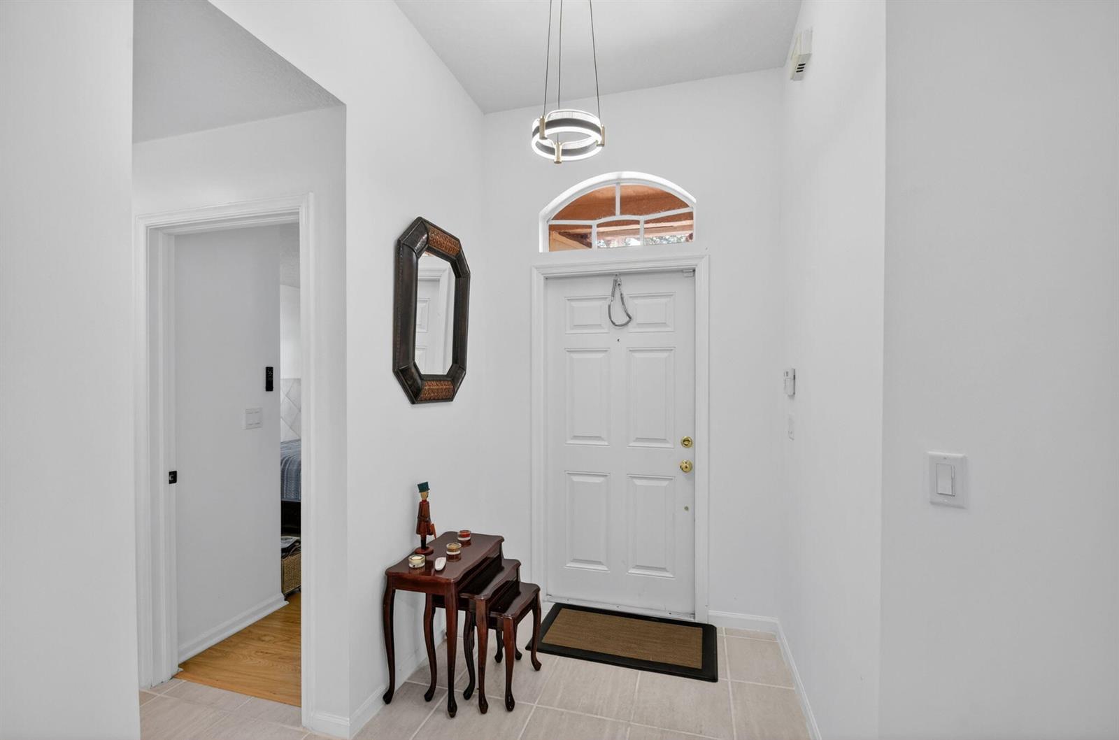 A bright entryway features a white front door, tile flooring, and a small wooden table — 1084 Aspri Way, Riviera Beach FL 33418, RIVIERA BEACH, FL
