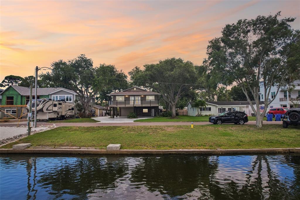 A two-story house with a raised deck sits behind a grassy lawn and a canal — 300 90TH AVENUE NE, ST PETERSBURG, FL