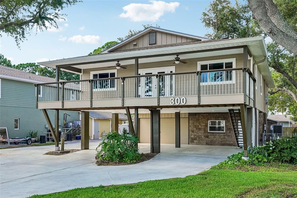 A two-story elevated house with a large wooden deck and a concrete ground-level carport — 300 90TH AVENUE NE, ST PETERSBURG, FL