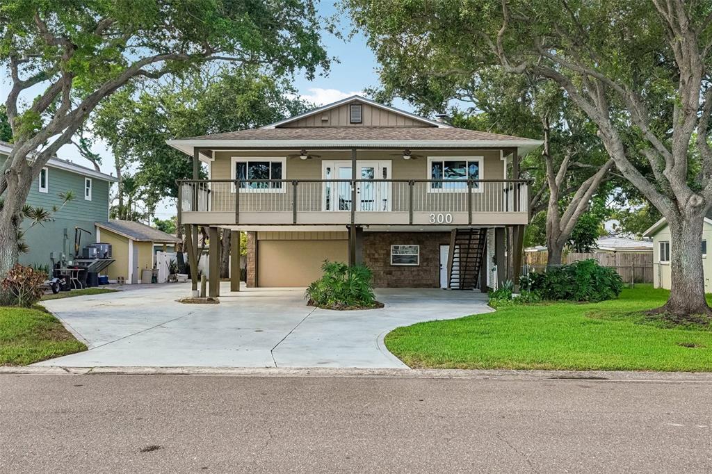 A two-story elevated house with a concrete driveway, wooden deck, and stone-accented ground level — 300 90TH AVENUE NE, ST PETERSBURG, FL