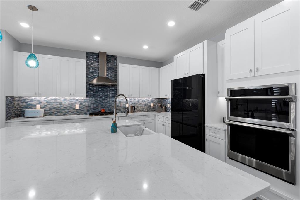 A modern kitchen features white cabinetry, a large quartz island, and a blue tiled backsplash — 5344 WISHING ARCH DRIVE, APOLLO BEACH, FL