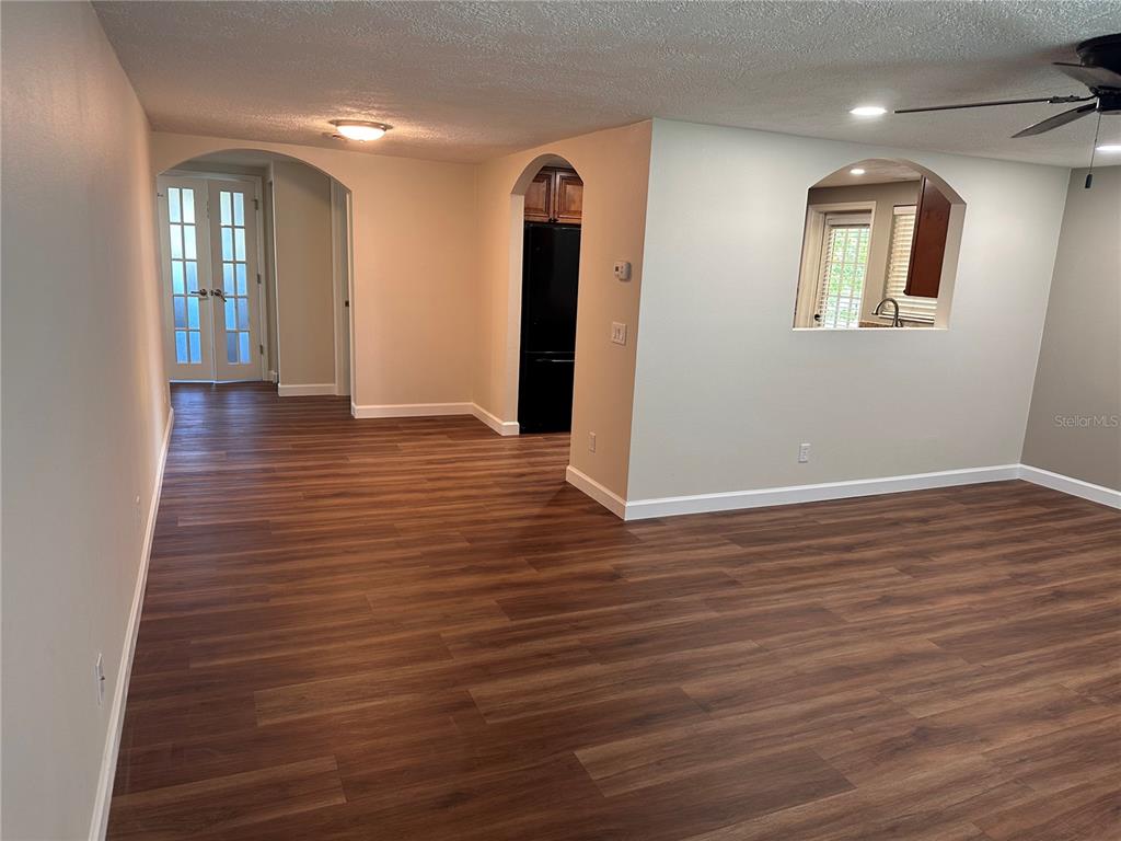 An interior view shows a room with wood-look flooring, arched doorways, and a kitchen pass-through — 855 STEWART STREET, ENGLEWOOD, FL