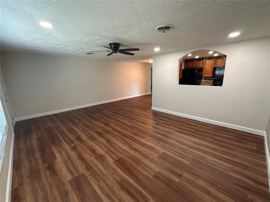 An empty living room features wood-look flooring, a ceiling fan, and a kitchen pass-through window — 855 STEWART STREET, ENGLEWOOD, FL