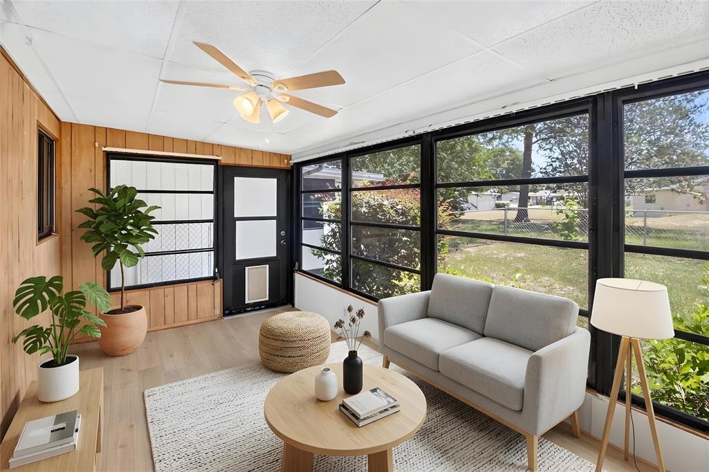 A sunroom features wood-paneled walls, light flooring, a ceiling fan, and large windows overlooking a yard — 10081 SW 95TH AVENUE, OCALA, FL