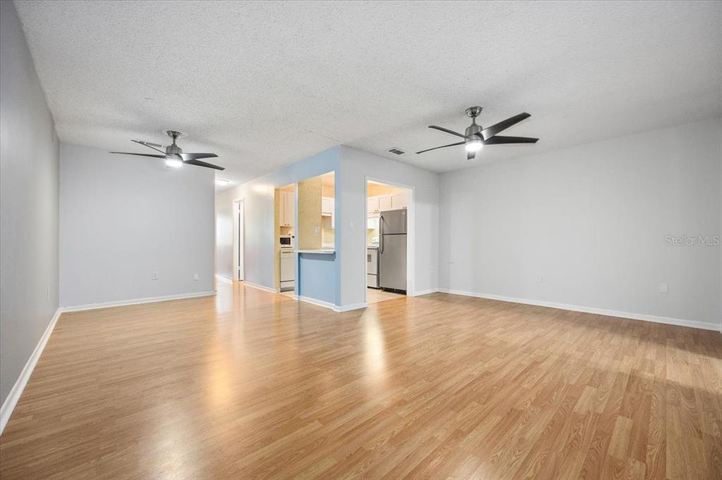An open-concept living area features light wood-look flooring, two ceiling fans, and a kitchen view — 2628 SW 14TH DRIVE UNIT 326, GAINESVILLE, FL