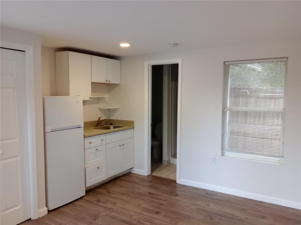A small kitchenette with white cabinets and a refrigerator sits next to a bathroom doorway — 4748 US HIGHWAY 17 UNIT 14, DE LEON SPRINGS, FL