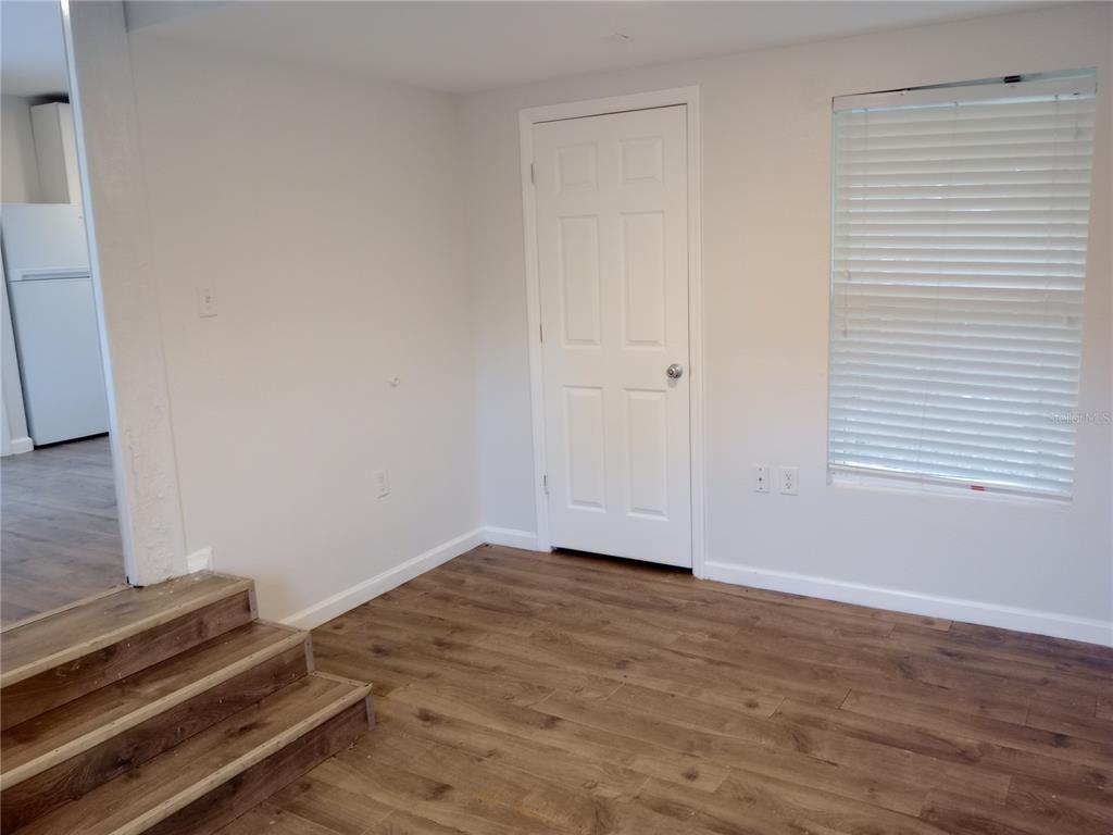 A room with wood-look flooring, a white door, a window with blinds, and wooden stairs — 4748 US HIGHWAY 17 UNIT 14, DE LEON SPRINGS, FL