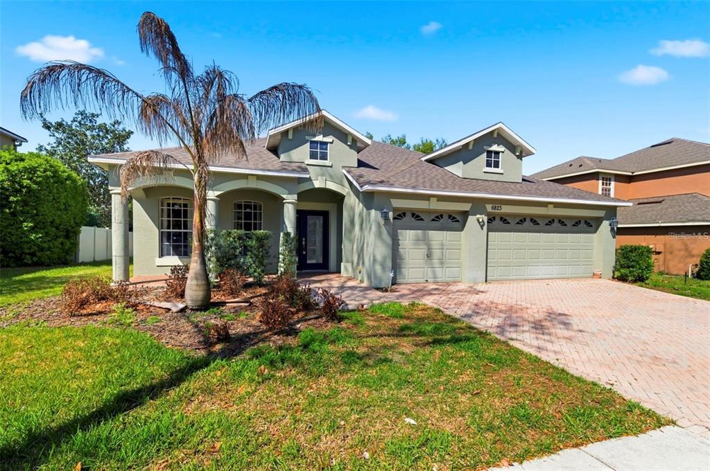 A single-story house with a beige exterior, a three-car garage, and a brick paver driveway — 6823 GREEN HERON DRIVE, WESLEY CHAPEL, FL