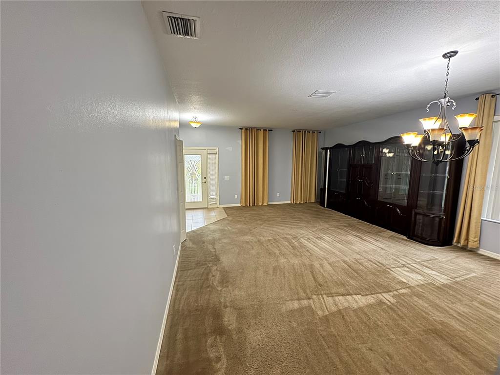 A spacious room features beige carpeting, light blue walls, a large dark hutch, and chandelier — 6823 GREEN HERON DRIVE, WESLEY CHAPEL, FL