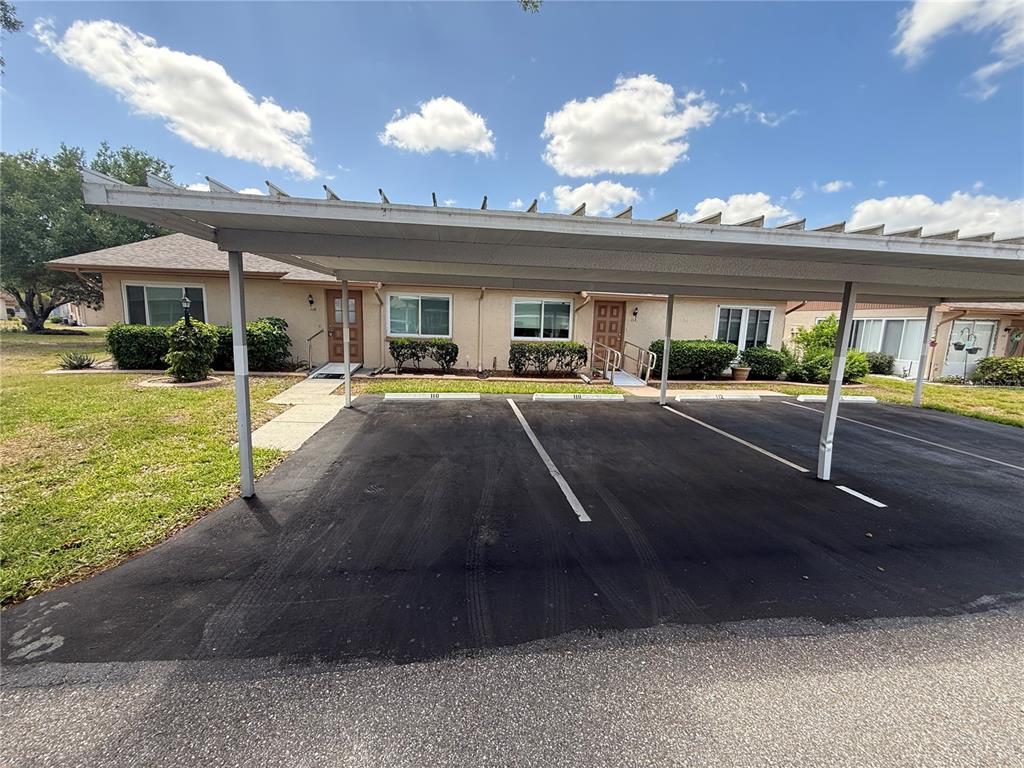 A single-story residential building with a metal carport covering four marked parking spaces — 110-112 GLOUCESTER BOULEVARD, SUN CITY CENTER, FL