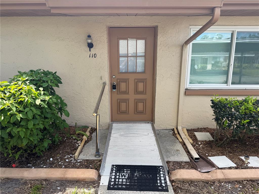 The exterior of a residential unit features a brown door, a ramp, and a handrail — 110-112 GLOUCESTER BOULEVARD, SUN CITY CENTER, FL