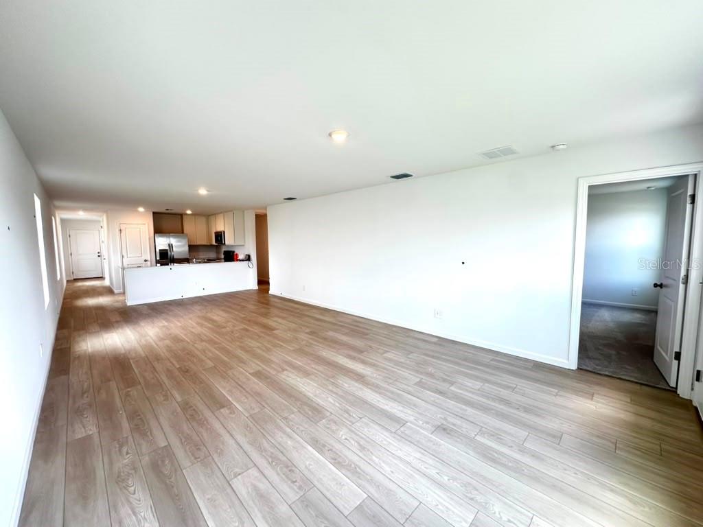 An open-concept living area with light wood-look flooring and a kitchen in the background — 5602 MORANT BAY PATH, KISSIMMEE, FL